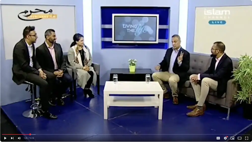Five people are seated in a TV studio set, engaged in a discussion. A screen behind them displays the program title "Living the Life.