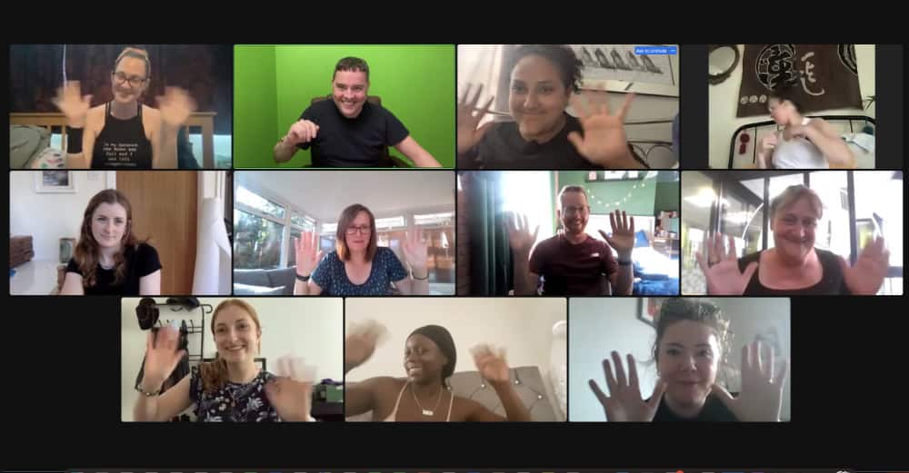 Screenshot of a virtual meeting with twelve people in separate video boxes, all smiling and waving at their cameras.